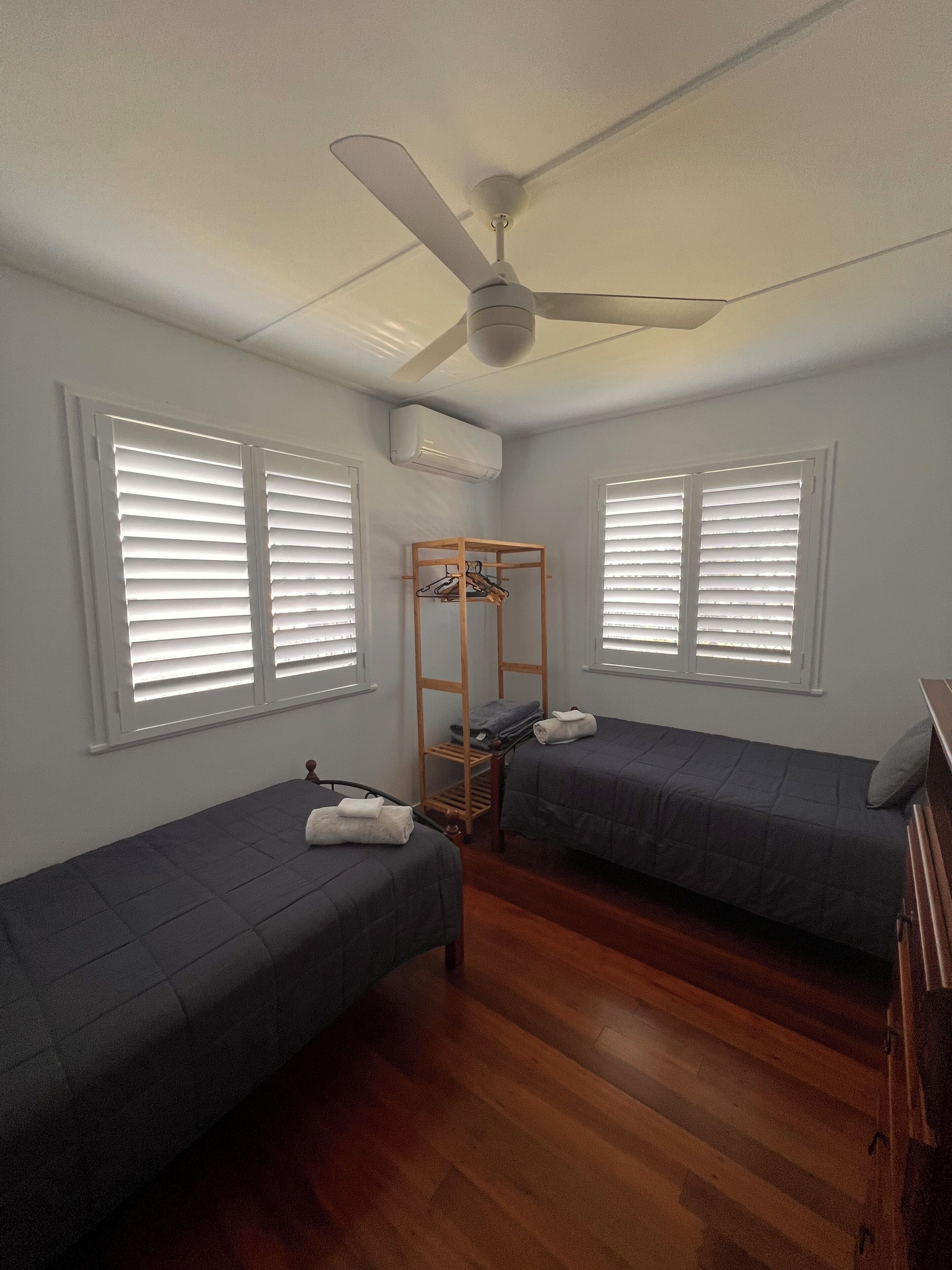 A room with two single beds, a ceiling fan, and an air conditioning unit.