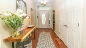 A hallway with a wooden bench, a vase of white flowers, a patterned rug, and a white door with a glass panel.