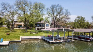 A lakeside property with a dock, a covered seating area, and a house in the background.