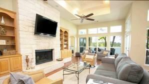 A spacious living room with a fireplace, comfortable seating, and large windows offering a view of the outdoors.