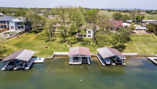 A lakeside property with three docked boats, a swimming pool, and a large lawn area.