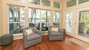 A spacious room with large windows, two patterned armchairs, a small ottoman, and a view of a deck with outdoor furniture.