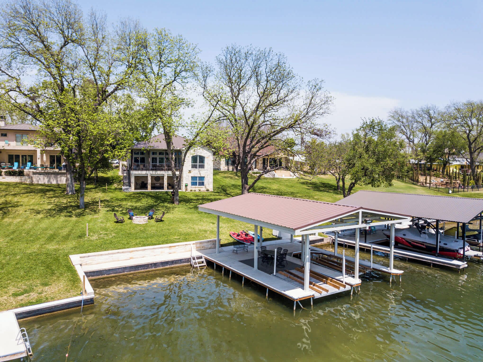 A lakeside property with a dock, outdoor seating, and a house in the background.