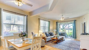 A spacious living room with a wooden dining table, chairs, a sofa, and a coffee table. There are large windows with curtains, a ceiling fan, and a view of the outdoors. - 5 Mi to JetBlue Park: Condo w/ Pool & Pickleball (Fort Myers)
