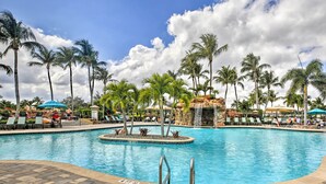 A swimming pool with lounge chairs and umbrellas, surrounded by palm trees. - 5 Mi to JetBlue Park: Condo w/ Pool & Pickleball (Fort Myers)
