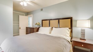 Un dormitorio con una cama grande, una mesita de noche con lámpara, un ventilador de techo y una puerta que da a otra habitación.