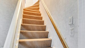 Una escalera alfombrada con barandilla blanca e interruptor de luz en la pared.