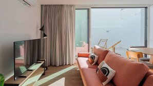 A modern living room with a flat-screen TV, a sofa with cushions, a dining table, and a large sliding glass door leading to a balcony. - Simple Life I, Setúbal (Setúbal)