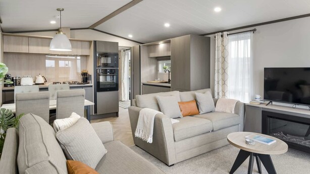 Una sala de estar moderna con sofá, mesa de centro y televisor. Cuenta con una zona de cocina con electrodomésticos y una mesa de comedor.