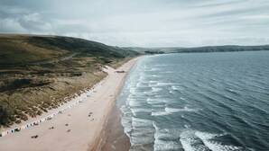 Una playa con una extensa franja de arena, una hilera de cabañas playeras y olas suaves.