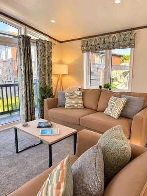A cozy living room with a sofa, a coffee table, and a lamp. There is a window with curtains and a view of the outside.