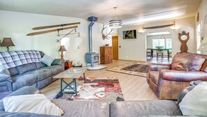A living room with a sofa, armchair, and a fireplace. There is a dining area in the background. - 11 Acres of Adventure! Woodsy Mead Stay w/ Trails (Mead)