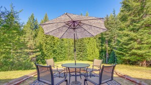 A round table with four chairs and a large umbrella in a forested outdoor area. - 11 Acres of Adventure! Woodsy Mead Stay w/ Trails (Mead)