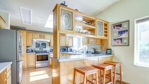 A kitchen with wooden cabinets, a stainless steel refrigerator, a microwave, and a coffee maker. There are two wooden stools at the island. - 11 Acres of Adventure! Woodsy Mead Stay w/ Trails (Mead)