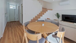 A modern living room with a round wooden table, grey upholstered chairs, a grey sofa, a staircase with wooden steps, and a flat-screen TV on a wooden stand. - Simple Life II, Setúbal (Setúbal)