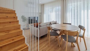 A modern living room with a wooden staircase, a round dining table with chairs, a sofa, and a TV. - Simple Life II, Setúbal (Setúbal)