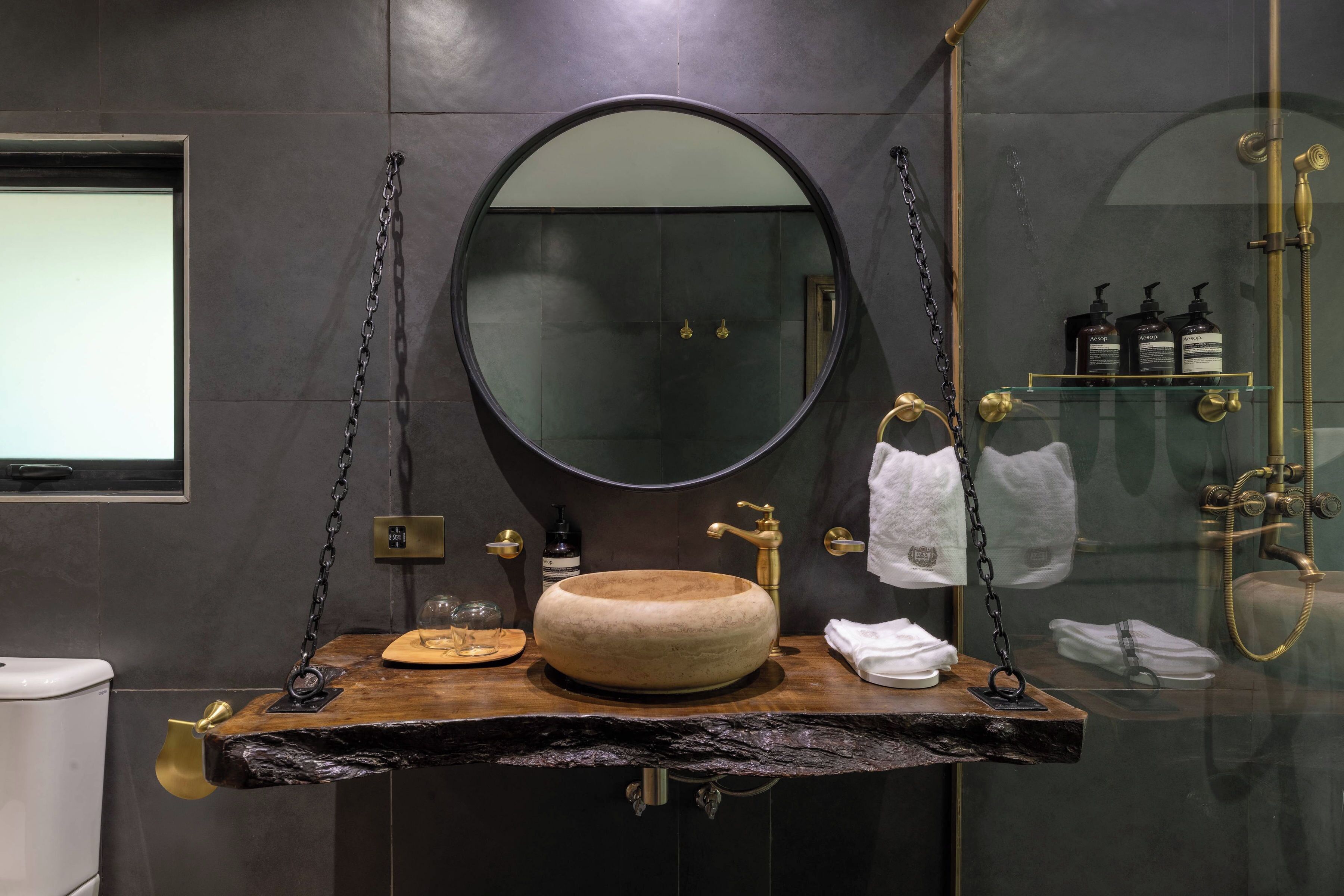 A modern bathroom with a round mirror, wooden vanity, and a glass shower enclosure.