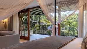 A bedroom with a bed, a sofa, and a view of a lush garden through large windows. - Pax Manor Muthaiga (Nairobi)