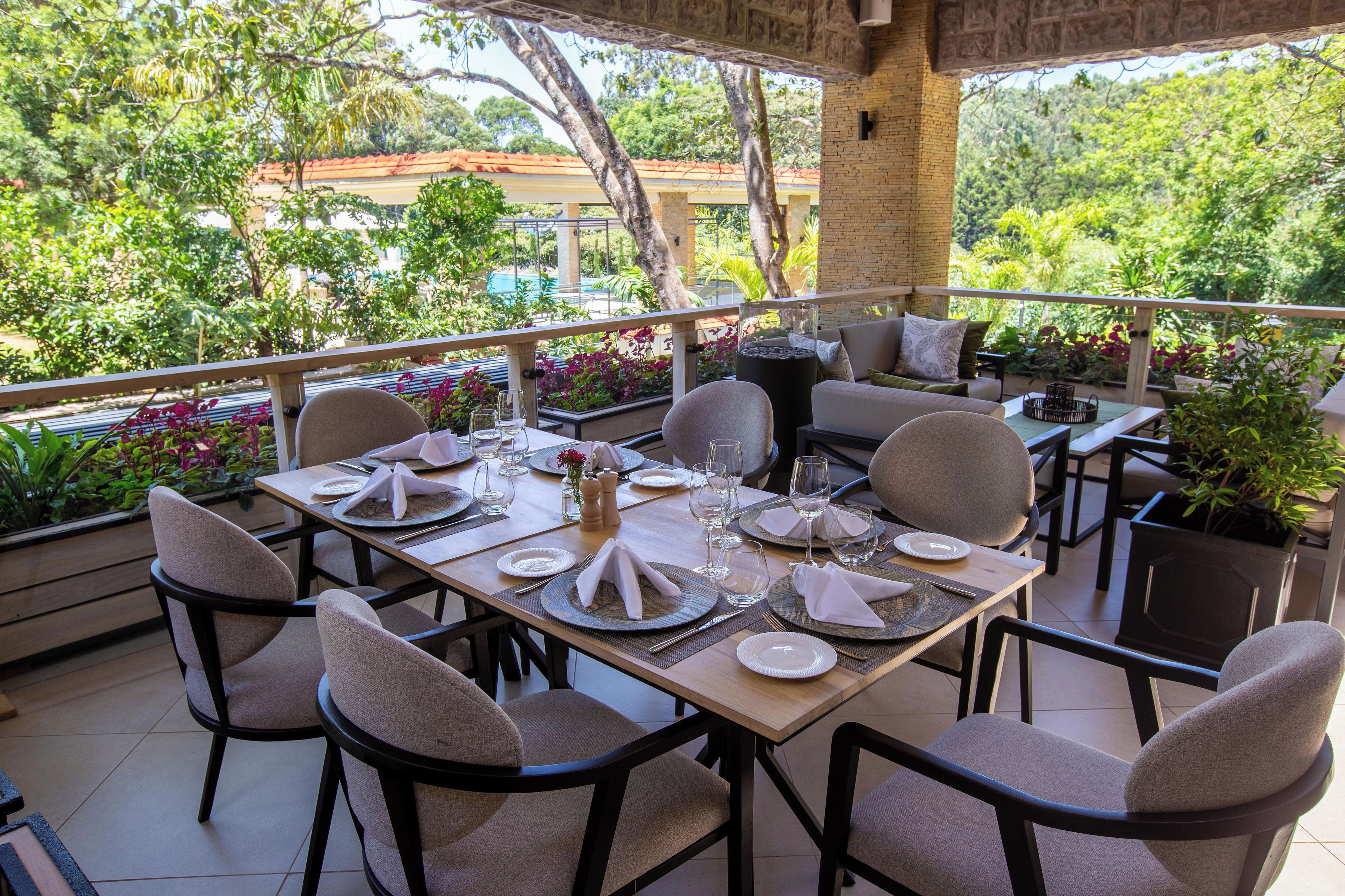 A dining area with tables set for four, surrounded by chairs, and overlooking a lush garden.
