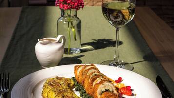 Un plato con comida, una copa de vino blanco, un florero con flores y una jarra pequeña sobre una mesa.
