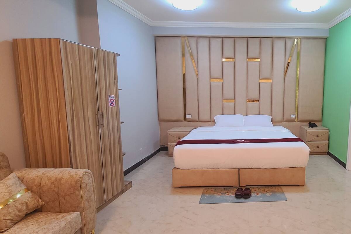 A bedroom with a bed, nightstands, a wardrobe, and two armchairs.