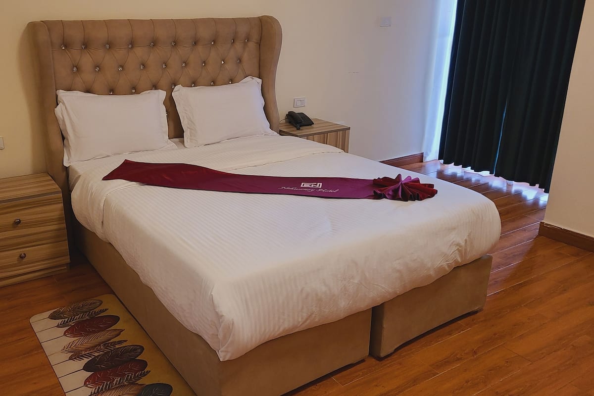 A neatly made bed with a white comforter and two pillows, a wooden nightstand with a phone, and a decorative pillow on the bed.