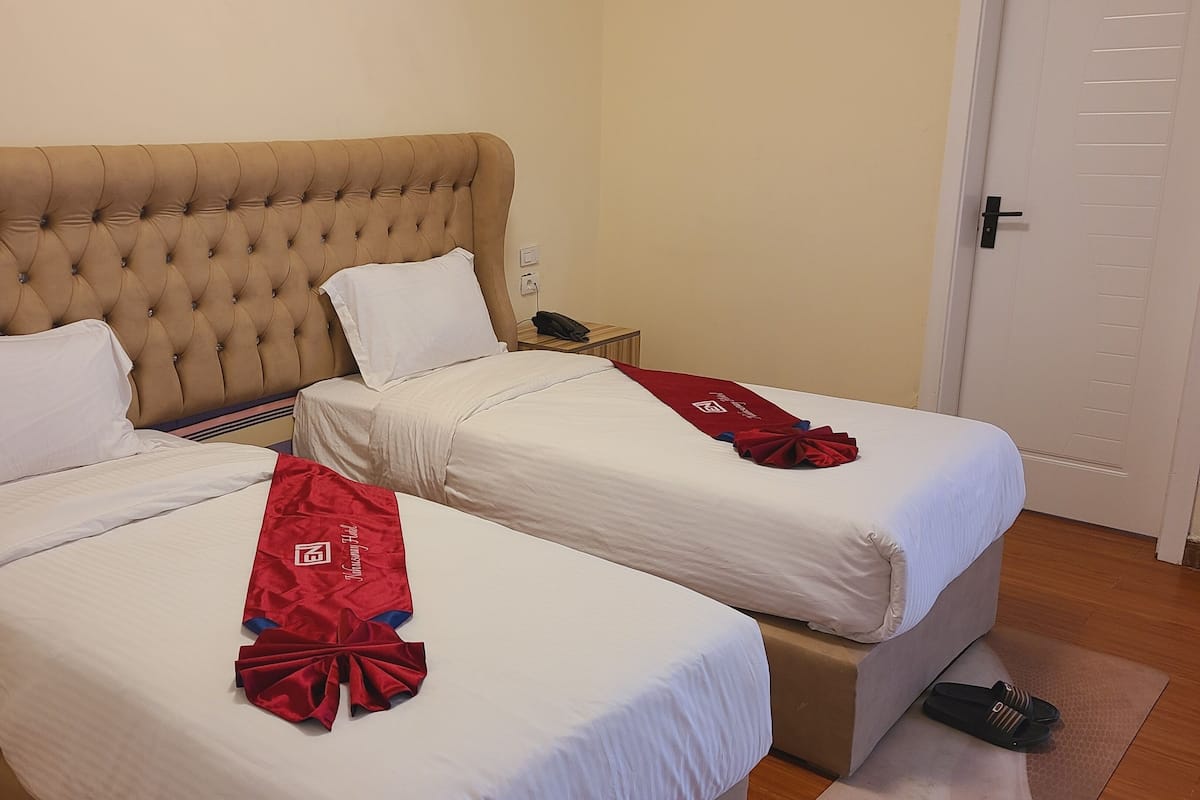 A hotel room with two beds, each with white linens and a red towel. There is a wooden nightstand with a phone and a lamp between the beds.