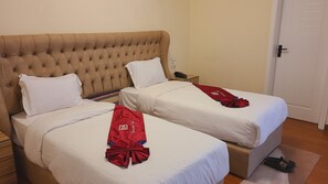 A hotel room with two beds, each with white linens and a red towel. There is a wooden nightstand with a phone and a lamp between the beds.