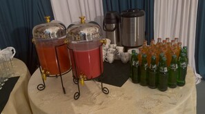 A buffet setup with two large punch dispensers, a coffee maker, and several bottles of soda.