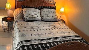 A bed with a patterned bedspread and two decorative pillows, flanked by two bedside lamps. - Bungalows in Guadeloupe ATOUMO (Petit-Canal)