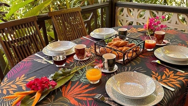 A tropical-themed dining table set with plates, cups, and a fruit basket. - Bungalows in Guadeloupe ATOUMO (Petit-Canal)