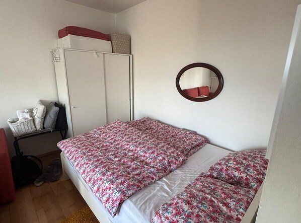 A bedroom with a bed, a wardrobe, a mirror, and a small table with a basket.
