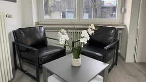 Et moderne værelse med to sorte lædersofaer, et hvidt bord og en vase med hvide blomster.