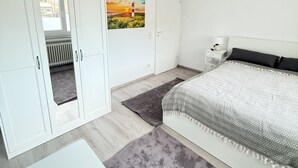 Et soveværelse med seng, garderobeskab, en dør med et billede og et vindue.