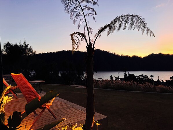 A wooden deck with a red chair and a table, overlooking a lake with a mountain in the background. - The Kamsha (Kintamani)