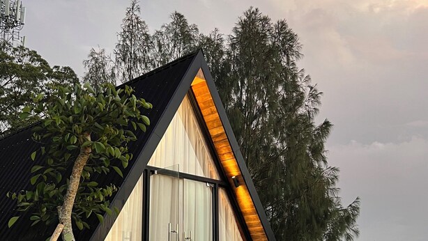 Ett modernt hus i form av en triangel, med en stor skjutdörr och en liten veranda med två trästolar.