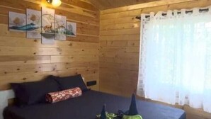 A wooden cabin bedroom with a bed, ceiling fan, and artwork on the wall.