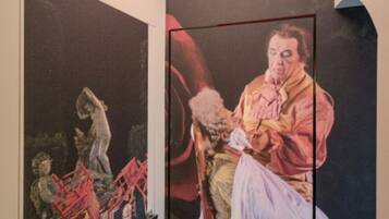 Une pièce dont un des murs est orné d’une grande fresque représentant une scène classique avec des personnages, et dont le plafond est éclairé par un luminaire rouge.