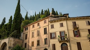 Un immeuble à plusieurs étages, doté d’une façade beige, de nombreuses fenêtres avec volets et d’un balcon orné de plantes en pot.