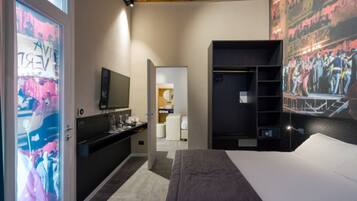 A hotel room with a bed, a TV, a vanity with a mirror, a wardrobe, and a wall with a mural.