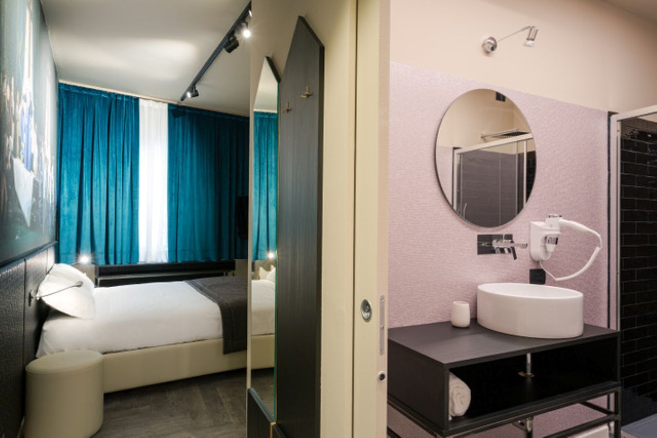 A hotel room with a bed, a large mirror, a round mirror above the sink, and a black tiled wall.