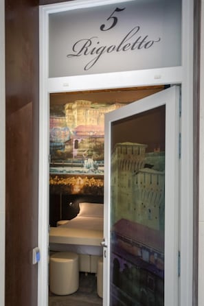 A hotel room with a bed, a small table, and a view of a historic building through a glass door. - Italianflat - Theatrum  (Verona)