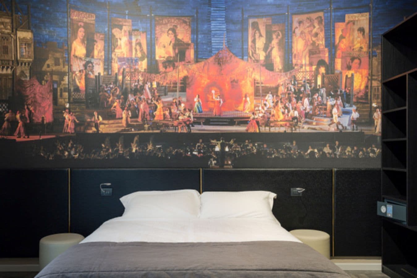 Een slaapkamer met een groot bed, een hoofdeinde met ingebouwde speakers en een muurschildering van een historisch tafereel.