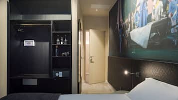 Ein Hotelzimmer mit Bett, Schrank, Ablage mit Flaschen und einem großen Gemälde an der Wand.