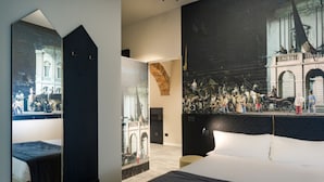 Une chambre d’hôtel moderne avec un grand lit, un miroir et un grand tableau représentant une scène historique.