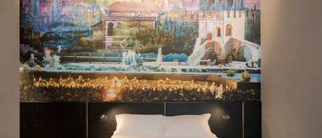 A bedroom with a large bed, a headboard with a mural, and two bedside lamps.