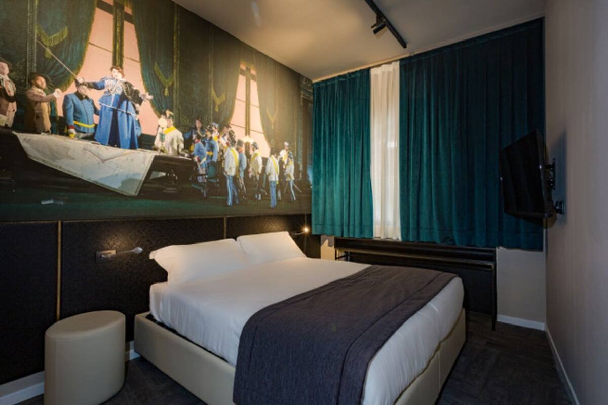 A hotel room with a large bed, a wall-mounted TV, and a mural depicting a historical scene.