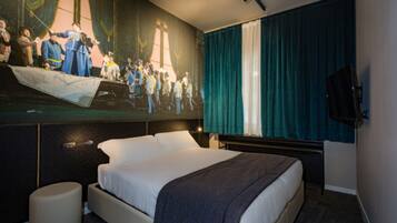 Ein Hotelzimmer mit einem großen Bett, einem an der Wand befestigten Fernseher und einem Wandbild, das eine historische Szene zeigt.