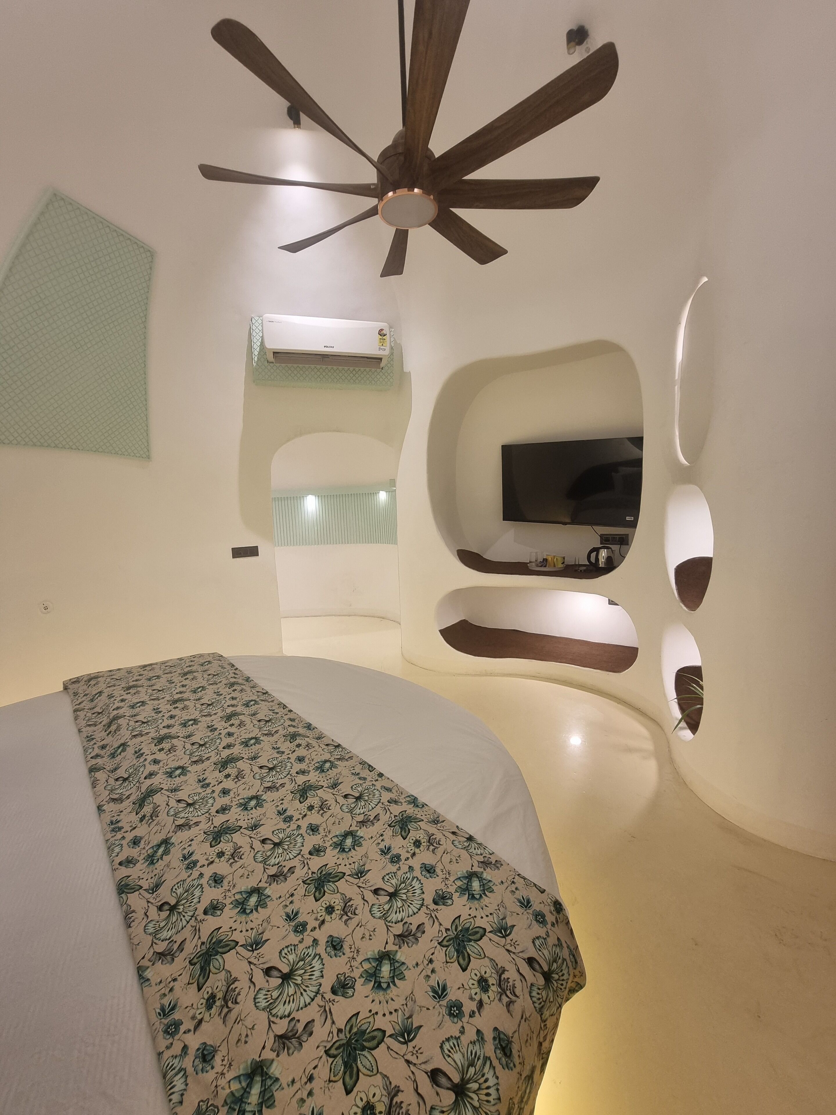 A bedroom with a bed, a ceiling fan, a TV, and a built-in shelf.
