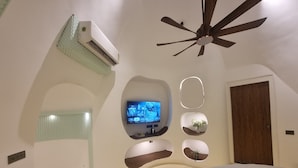 A bedroom with a bed, a ceiling fan, an air conditioning unit, a television, and wall-mounted planters. - Shridhar Reesort (Rishikesh)